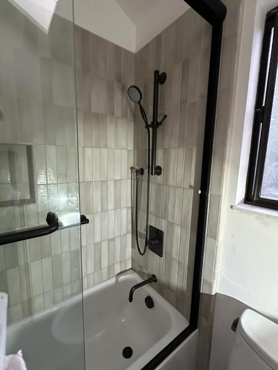 Tiled shower with glass door, matte black fixtures, and hand shower
